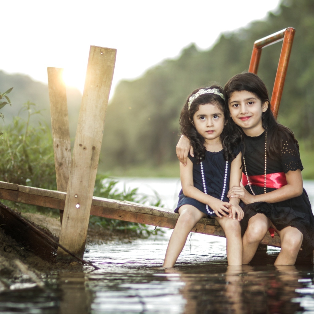 Две девочки сидят на мосту у реки