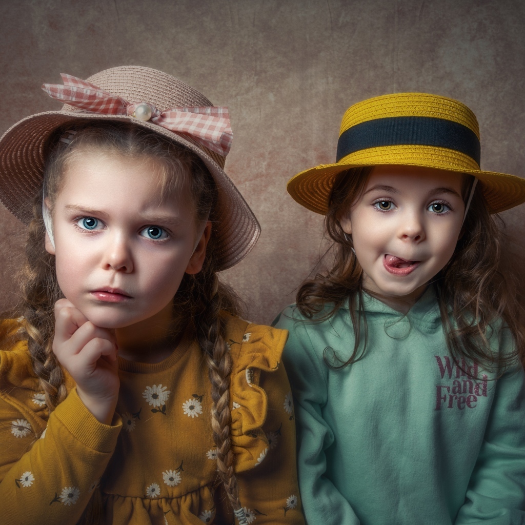Две маленькие девочки в шляпках на фоне коричневой стены