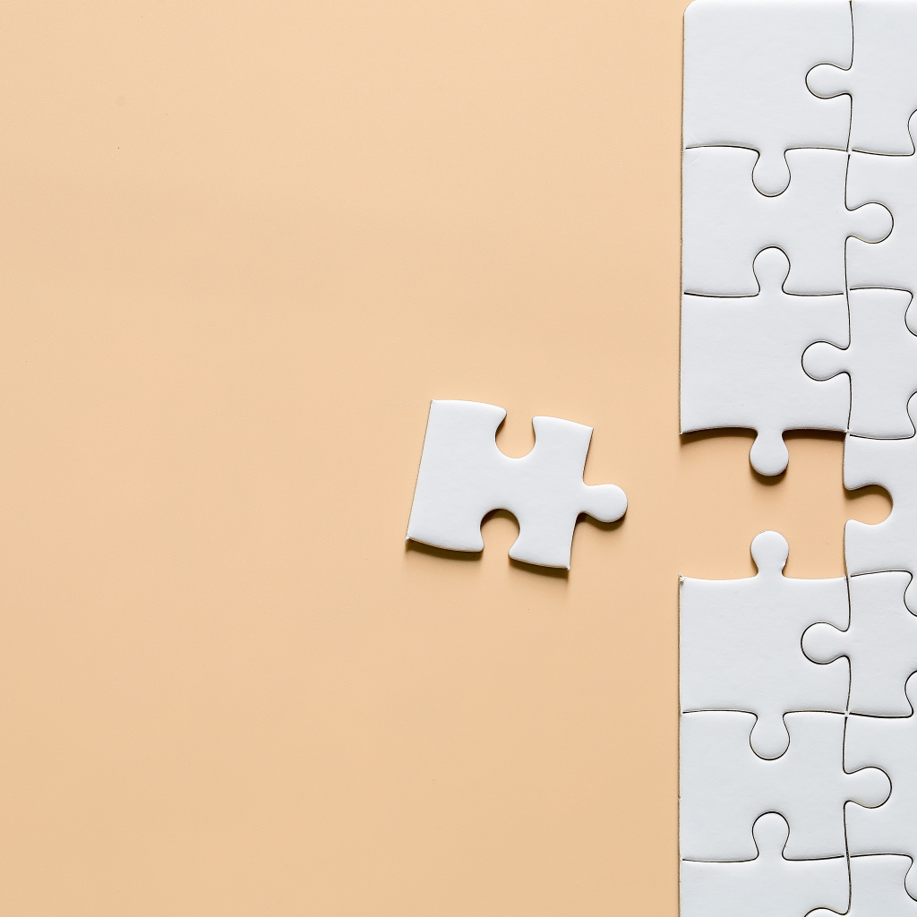 Белый пазл собирают на бежевом фоне