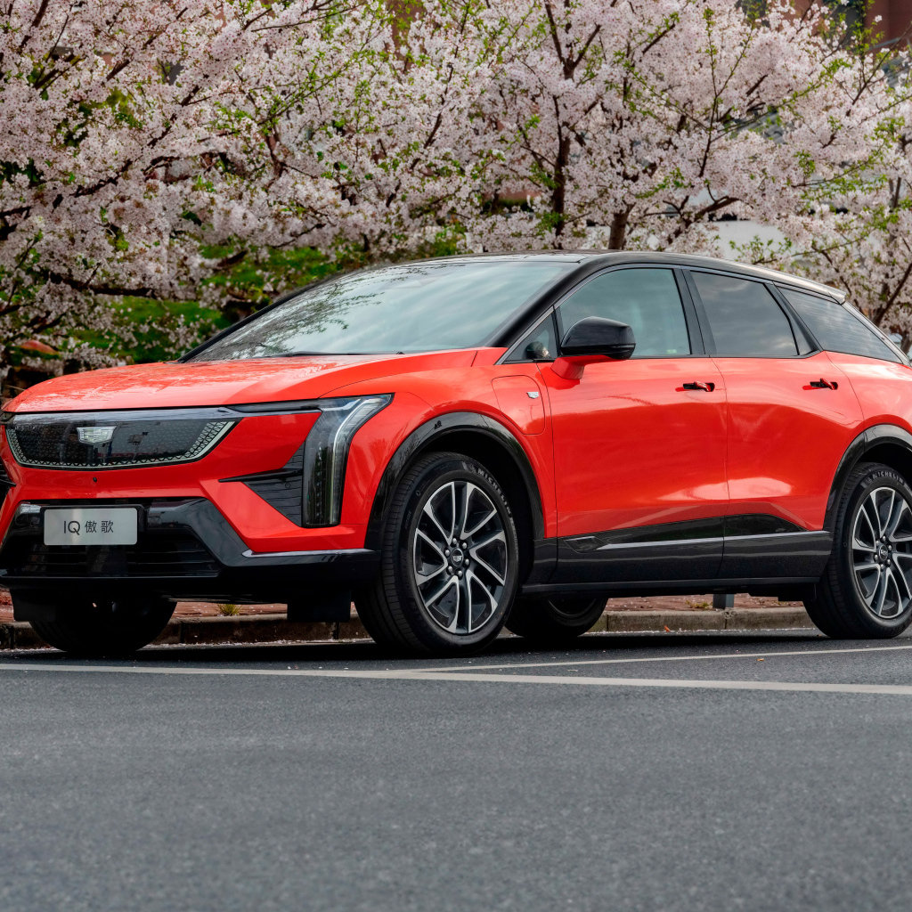 Красный Cadillac Optiq Sport 2024 года у цветущих деревьев