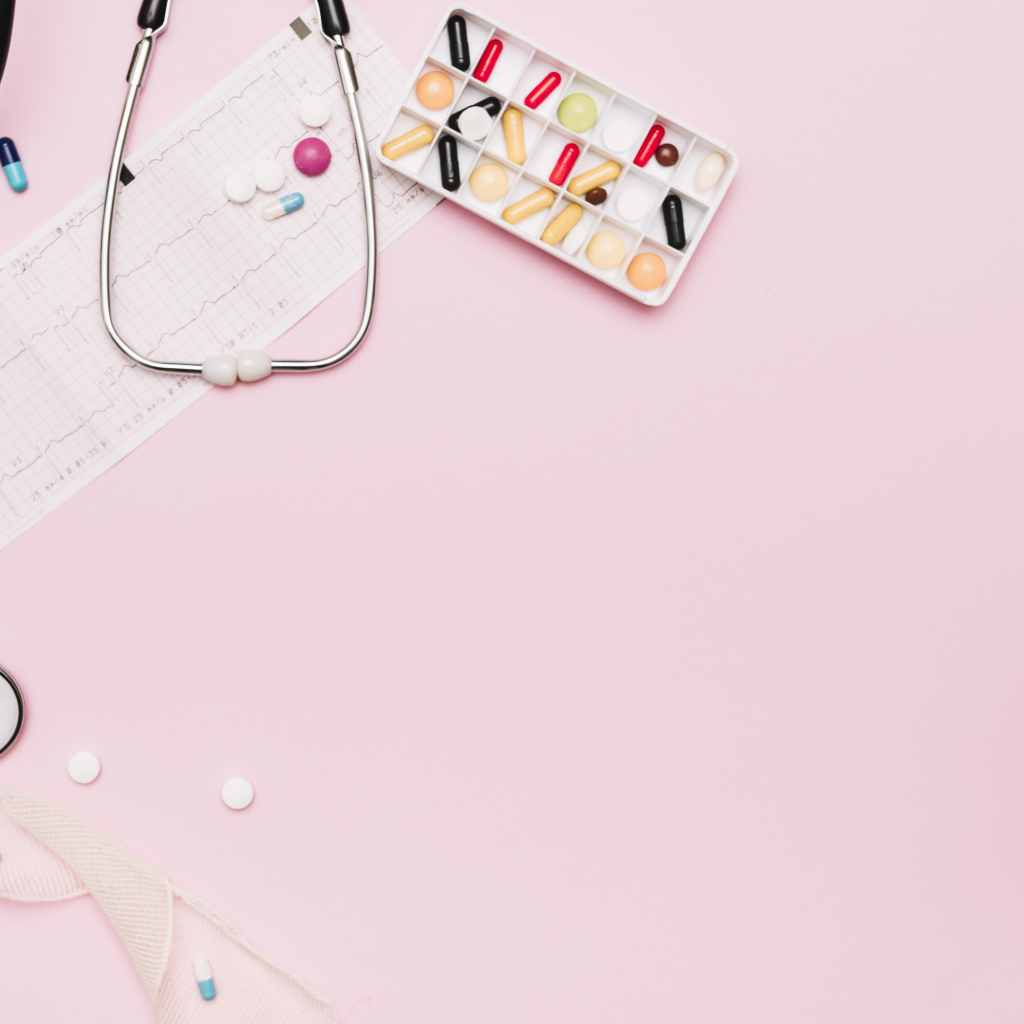 Стетоскоп и лекарства на кардиограмме на розовом фоне