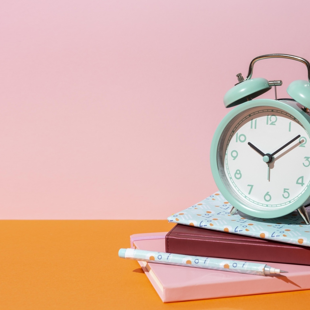 Будильник с книгами на розовом фоне