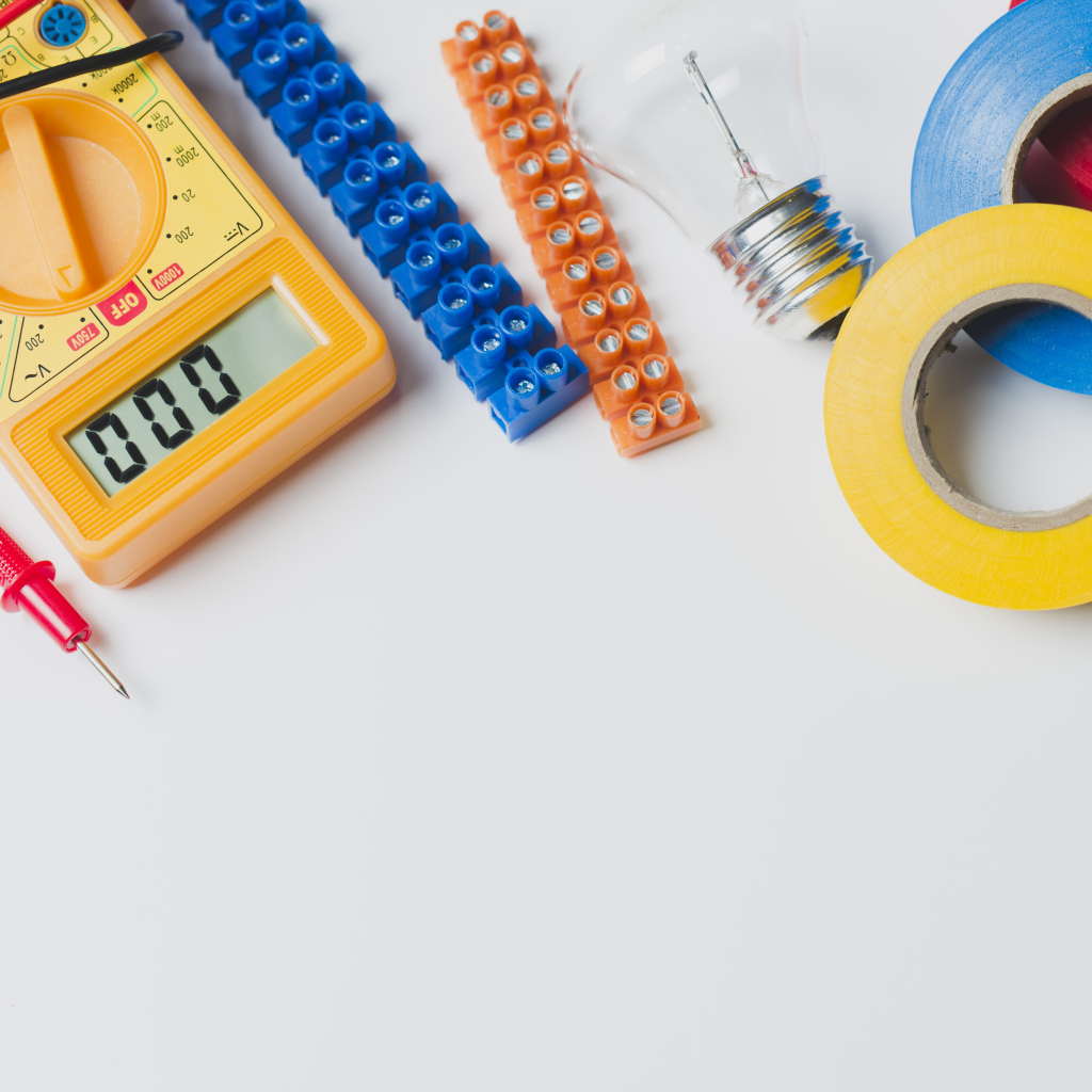 Электрическические приборы, мультиметр, изолента на сером фоне