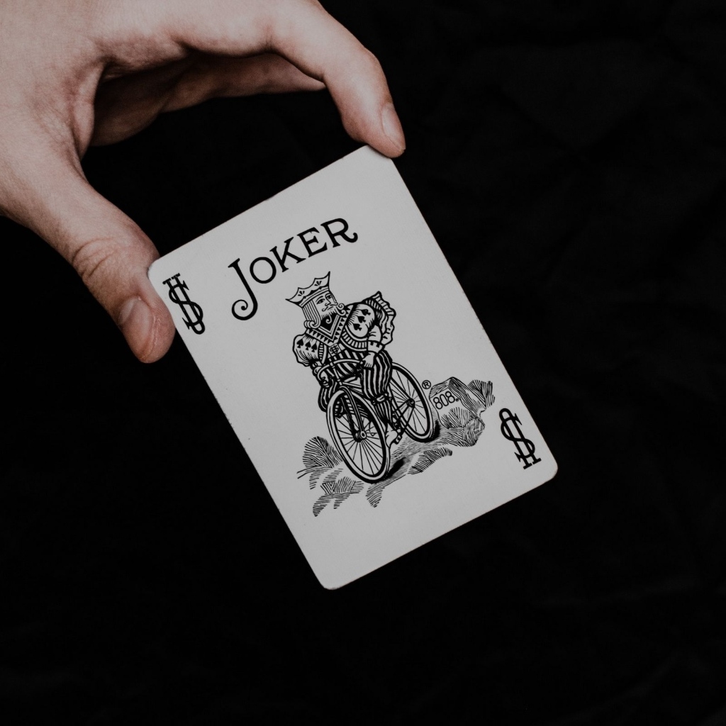 Карта Джокер в руке на черном фоне
