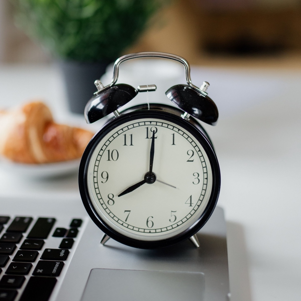 Большой черный будильник на столе у ноутбука