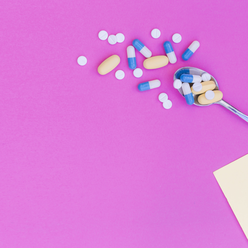 Таблетки с ложкой на розовом фоне