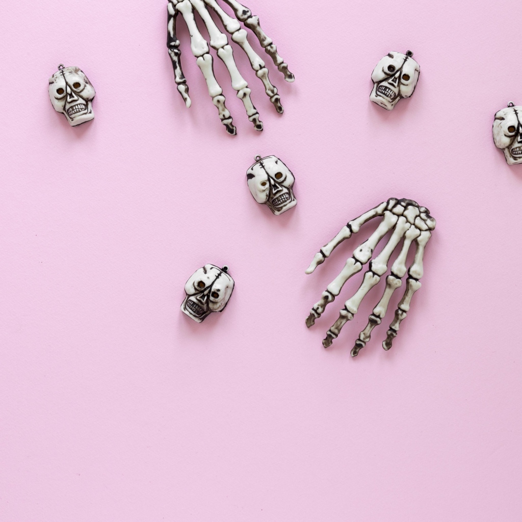 Кисти рук скелета и черепа на розовом фоне