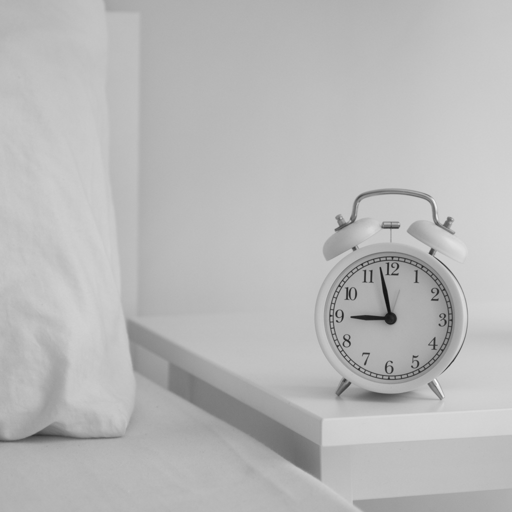 Будильник стоит на тумбочке у кровати 