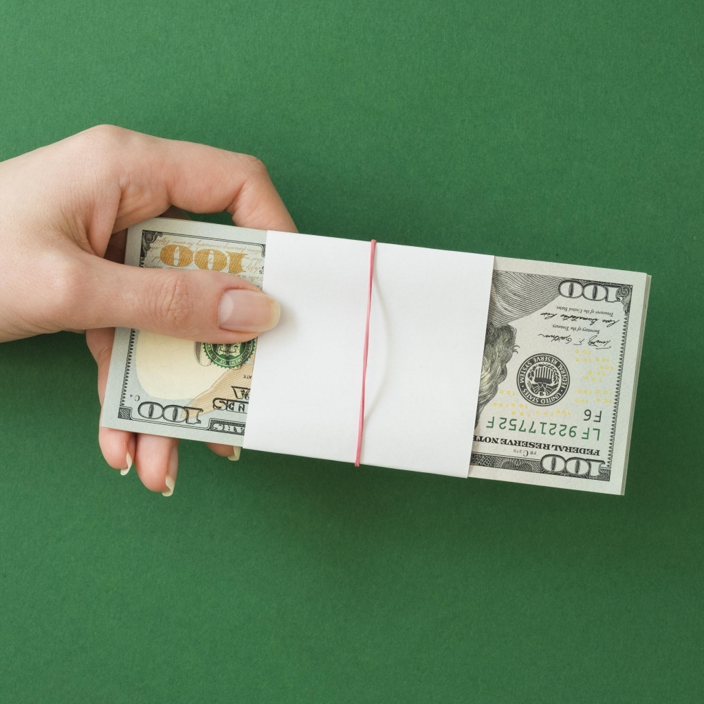 Пачка денег в руке у девушки на зеленом фоне