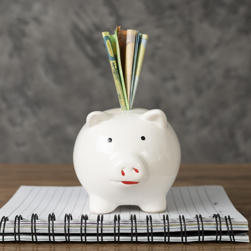 Свинья копилка с купюрами на столе с блокнотом