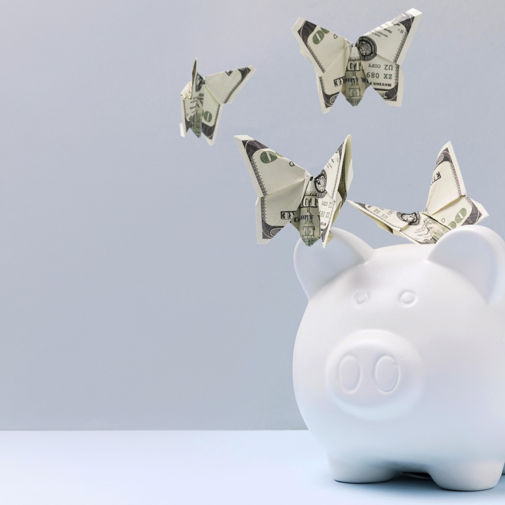 Свинья копилка с бабочками из купюр на сером фоне