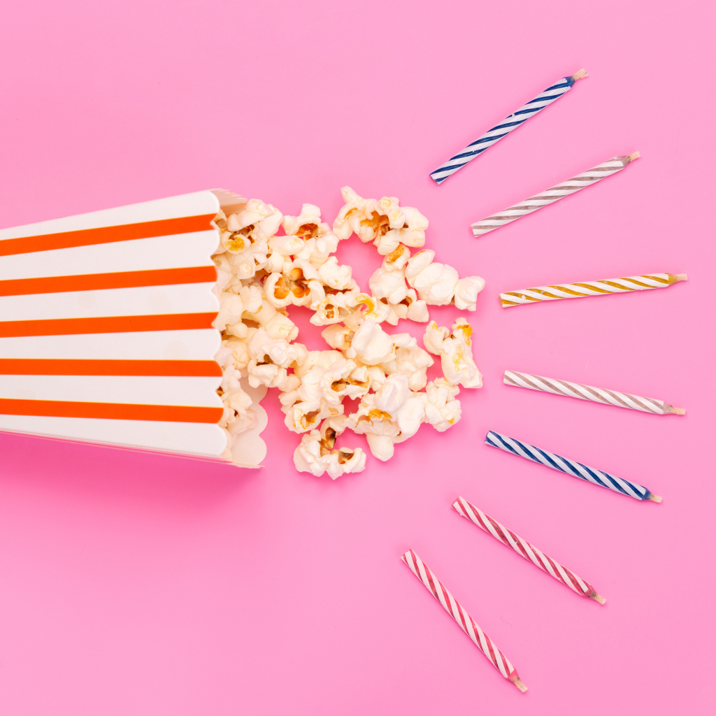 Коробка попкорна со свечами на розовом фоне