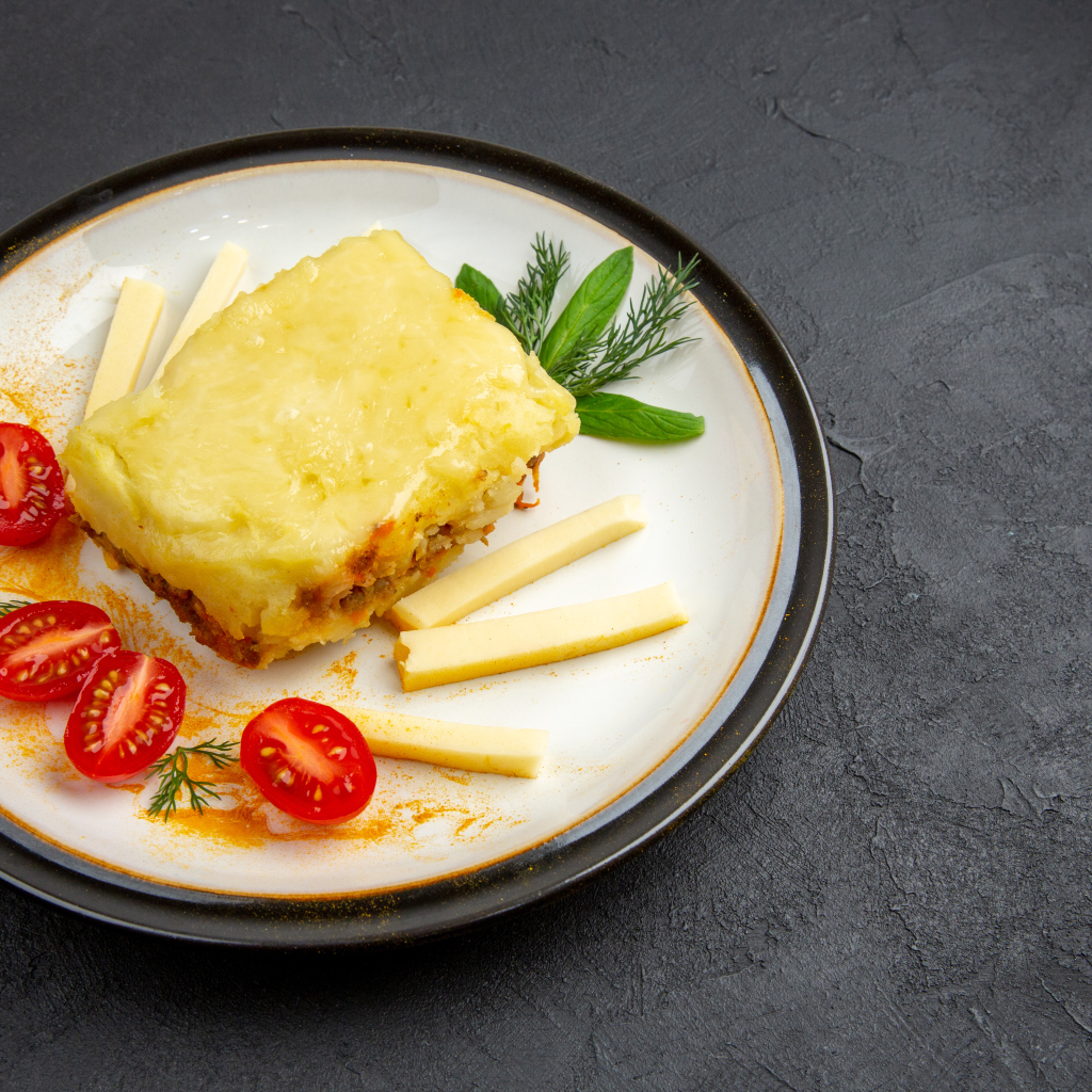 Кусок картофельной запеканки на тарелке с помидорами