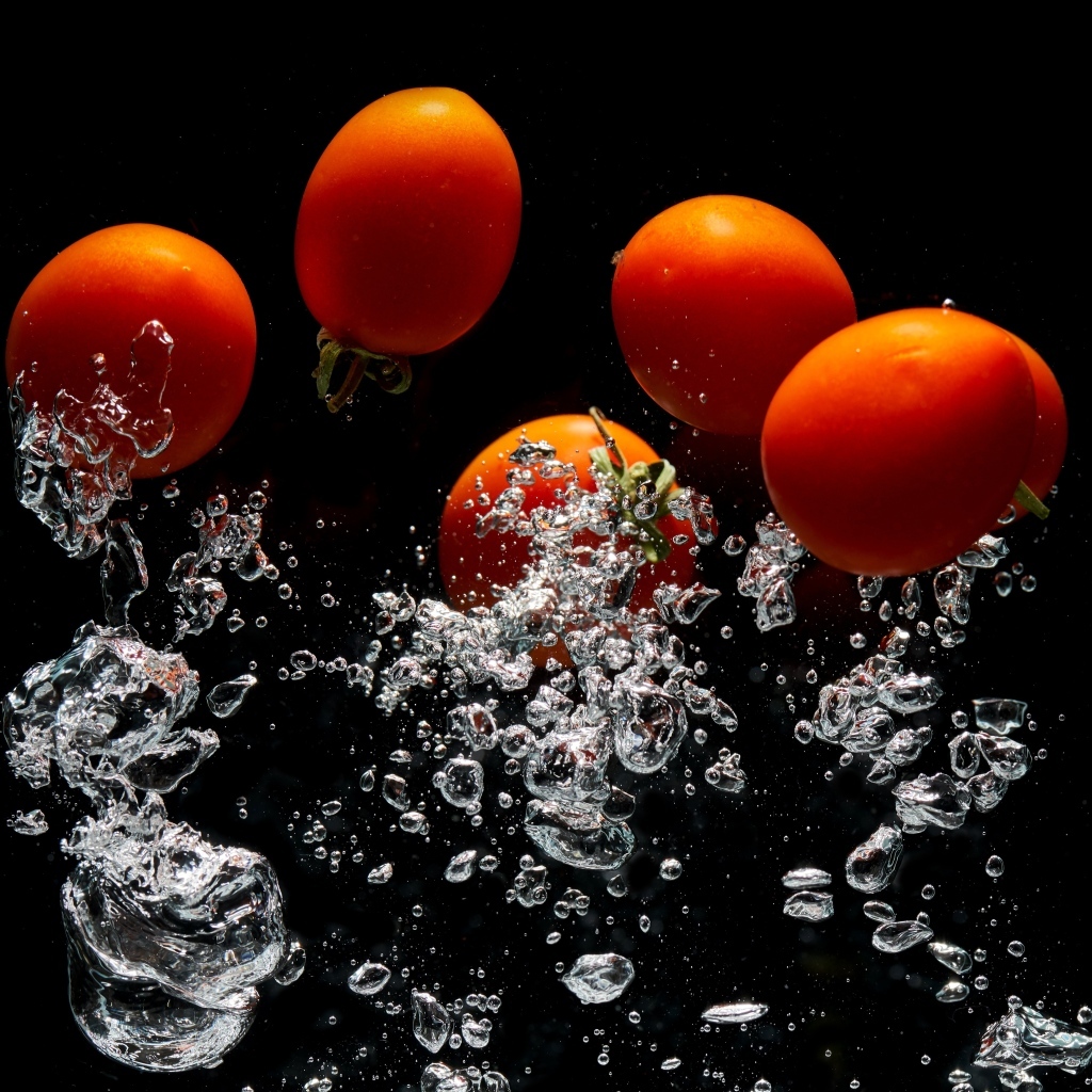 Красные помидоры в воде на черном фоне