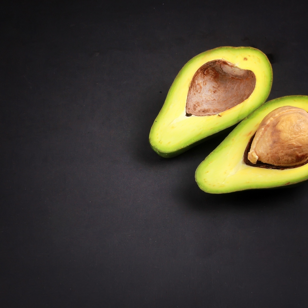 Свежий зеленый авокадо на черном фоне