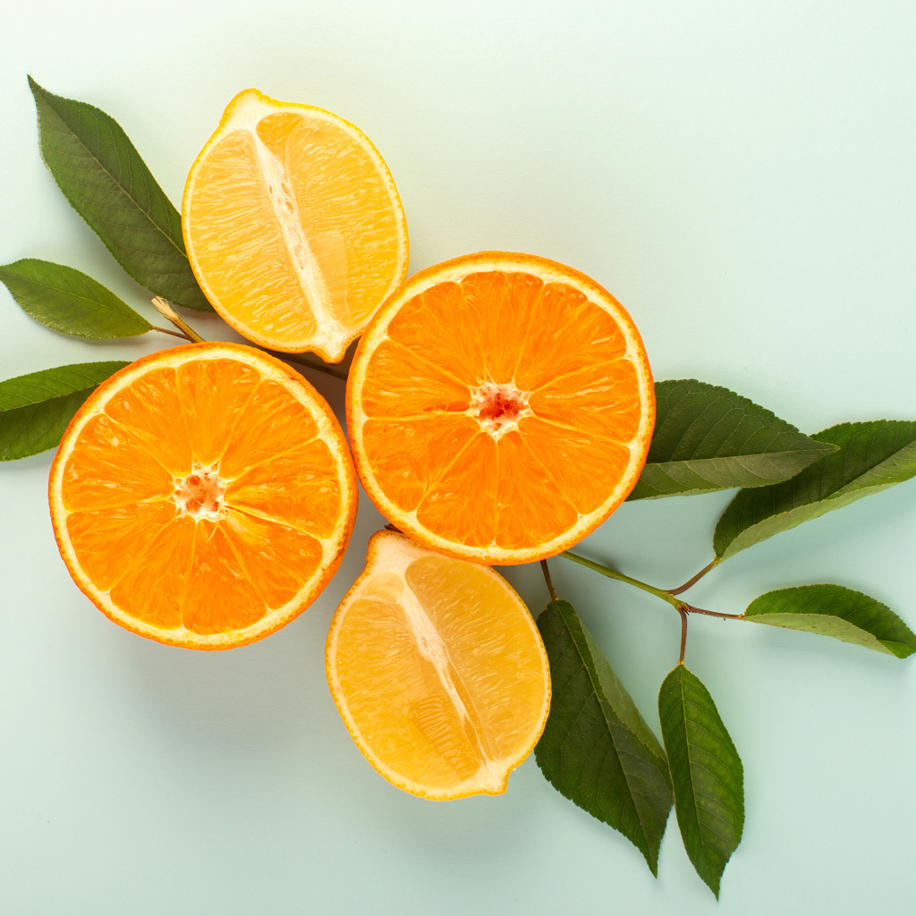 Половинки лимона и апельсина на столе с зелеными листьями