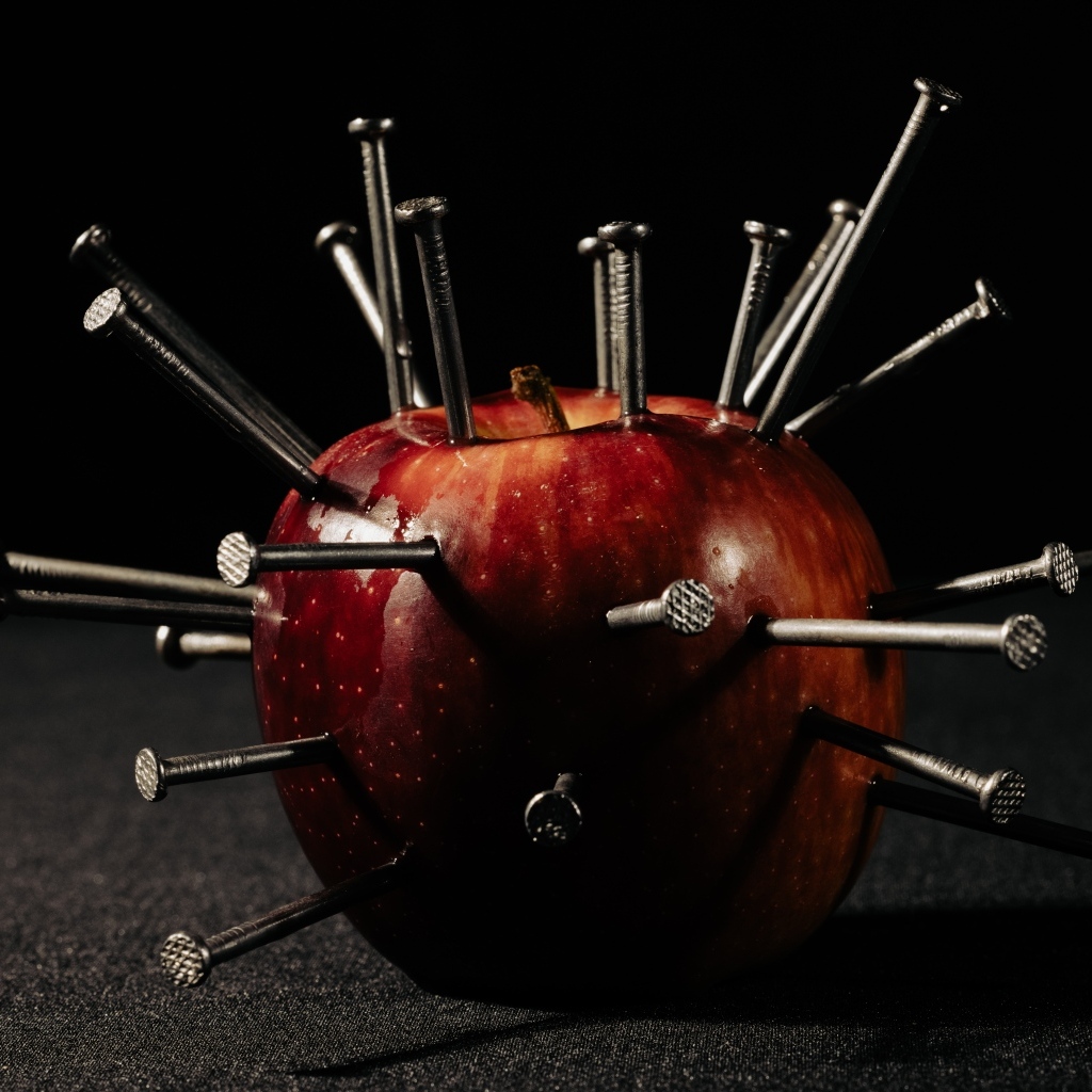 Красное яблоко утыканное гвоздями на темном фоне