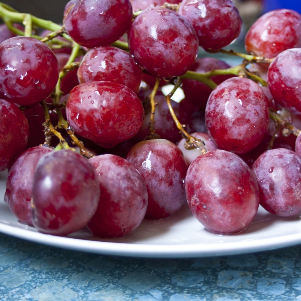 Спелый розовый виноград на белой тарелке