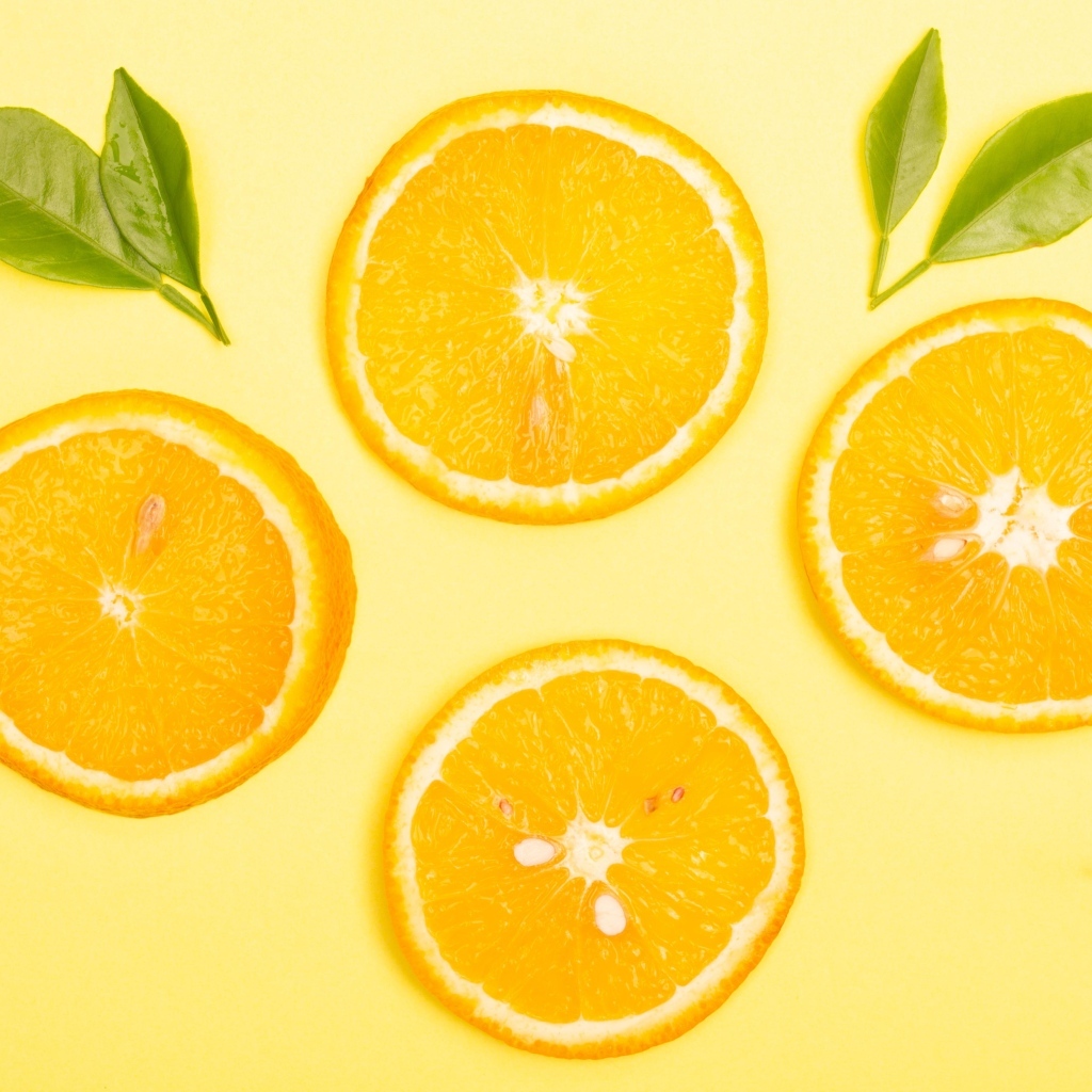 Нарезанный апельсин с зелеными листьями на желтом фоне