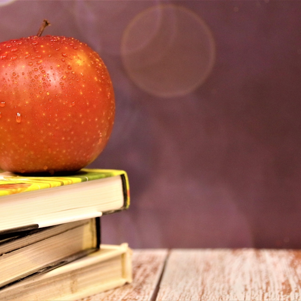 Мокрое яблоко на столе с книгами