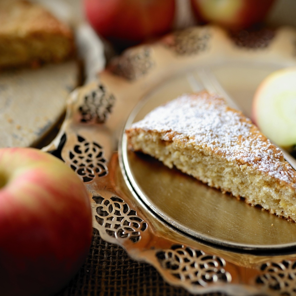 Кусок пирога с сахарной пудрой на столе с яблоками