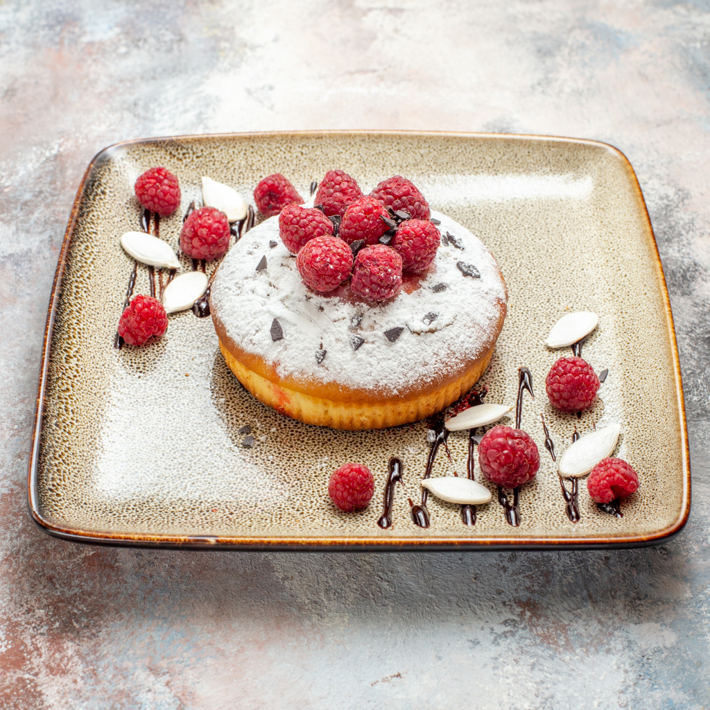 Пирожное с сахарной пудрой и малиной на тарелке