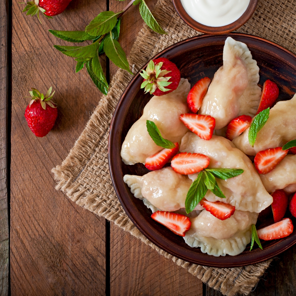 Вареники с клубникой на столе со сметаной