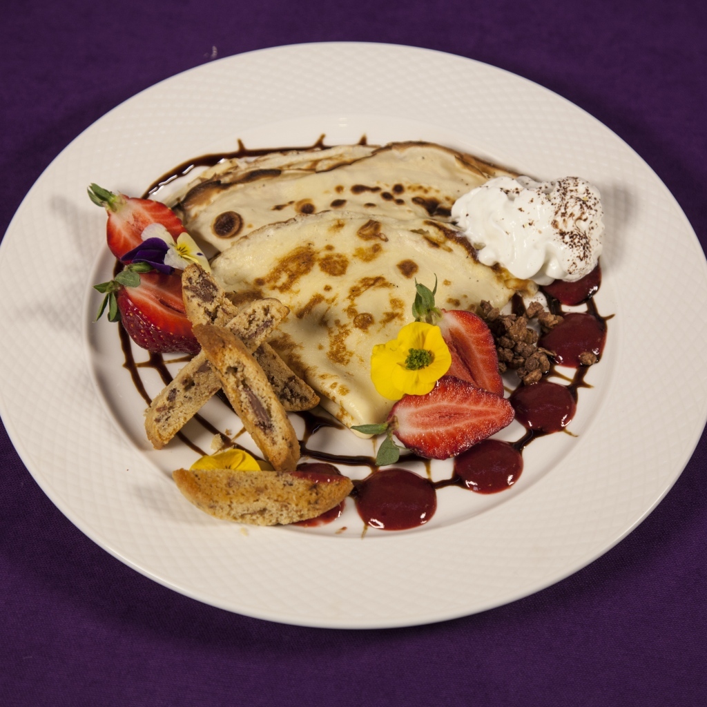 Тонкие блинчики с кремом и ягодами на тарелке