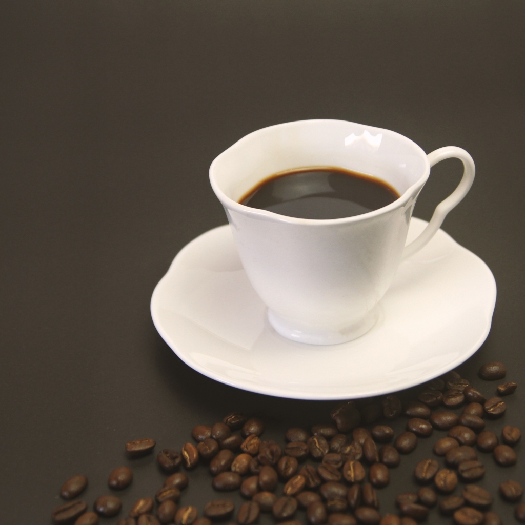 Белая чашка с кофе на столе с зернами