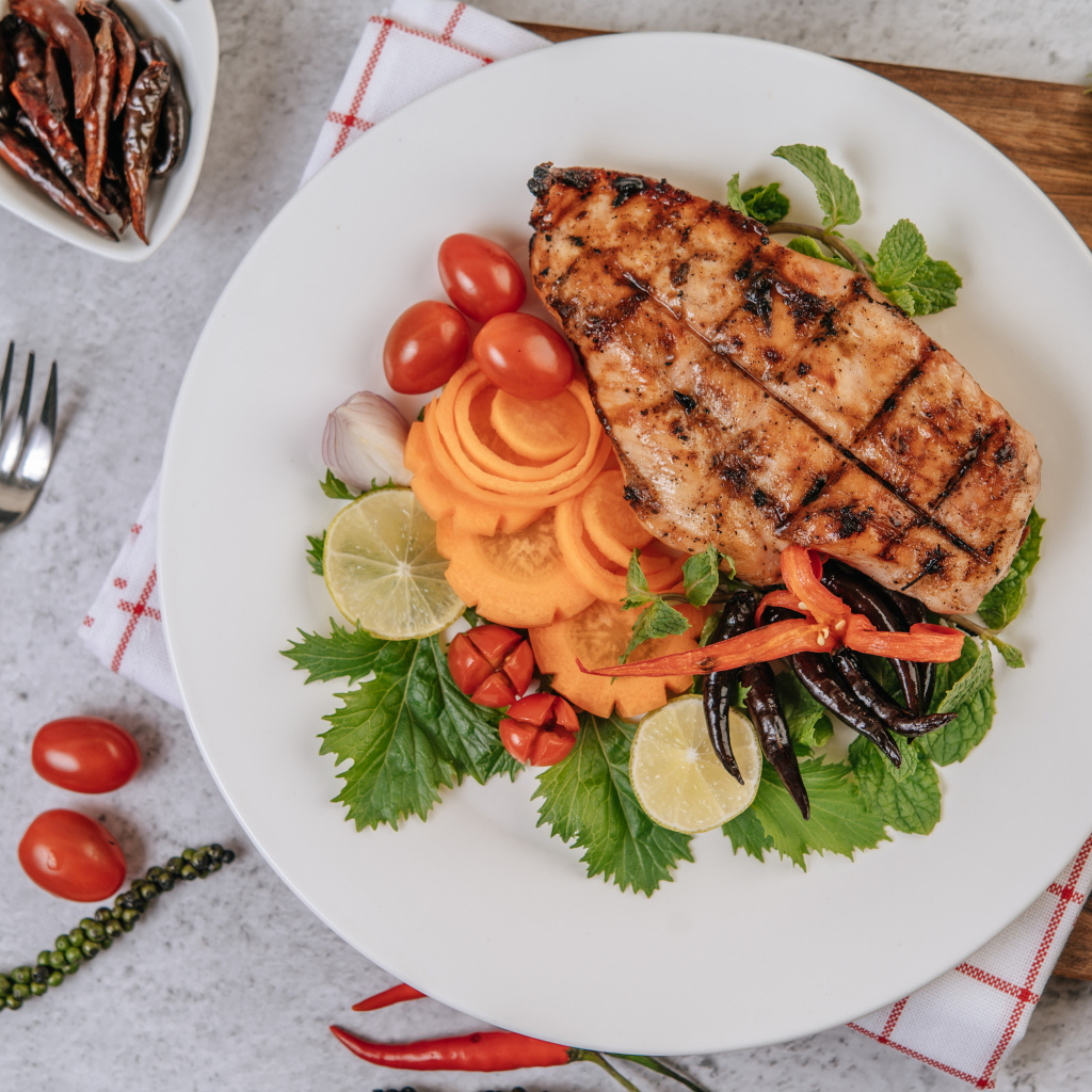 Кусок жареной курицы на большой белой тарелке с овощами