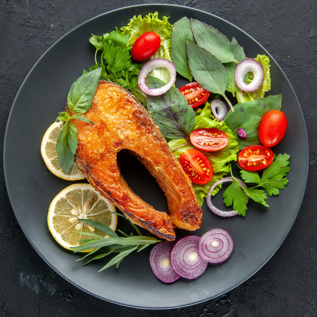 Жареная рыба на тарелке с зеленью,  лимоном и помидорами