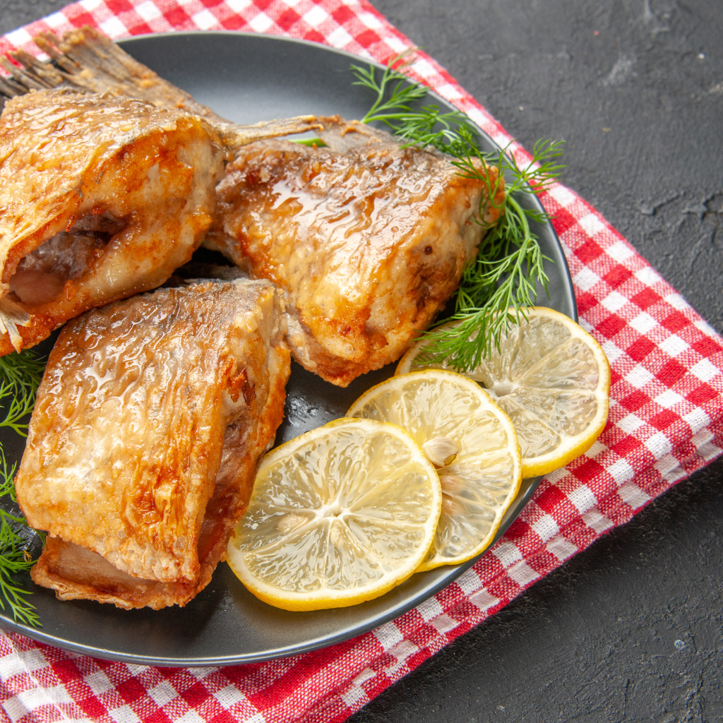 Куски жареной рыбы на тарелке с кусочками лимона и укропом