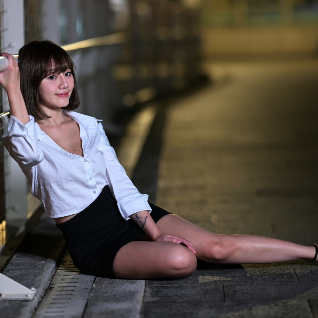 Девушка в черной юбке и белой рубашке сидит на дороге