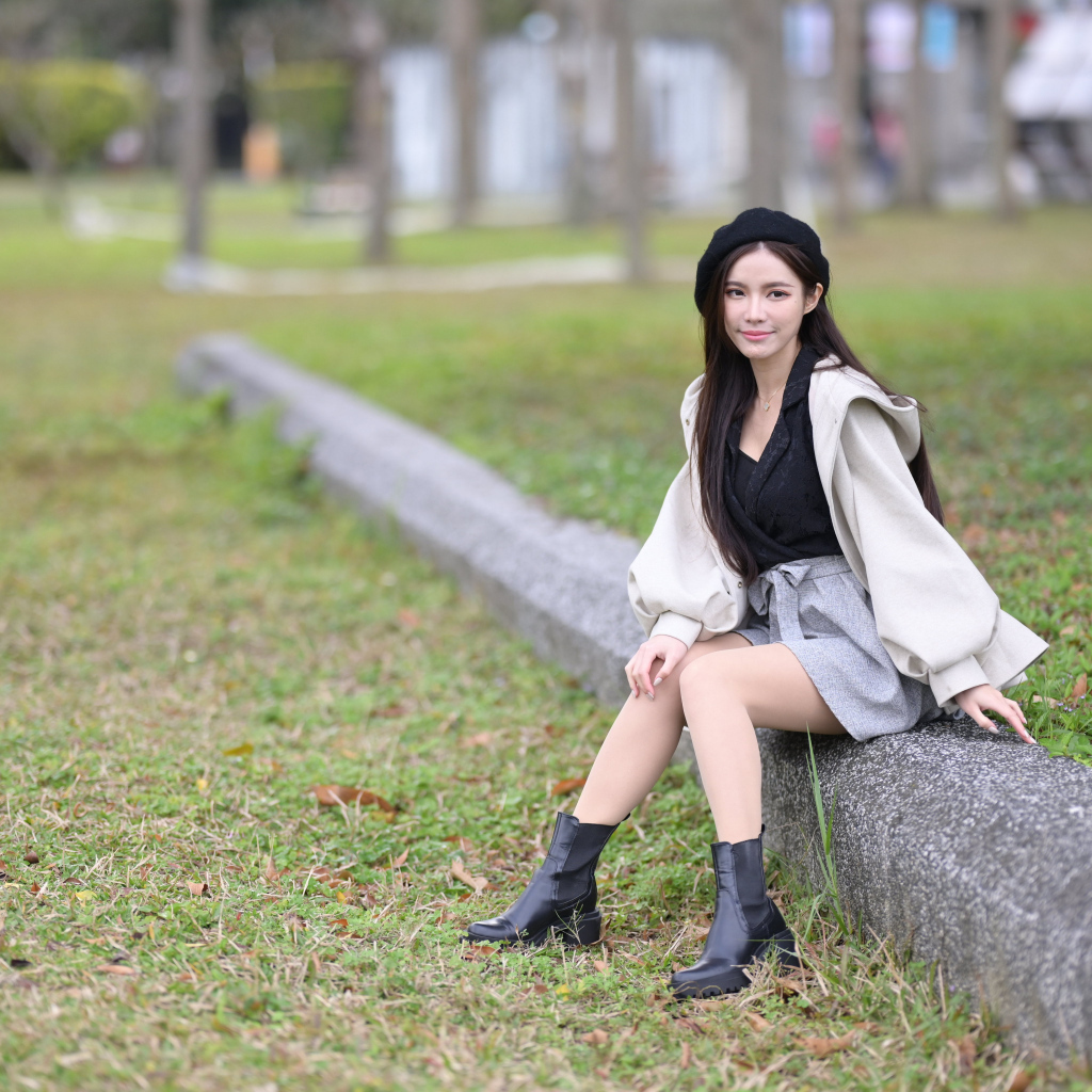 Девушка в пальто сидит на земле в парке