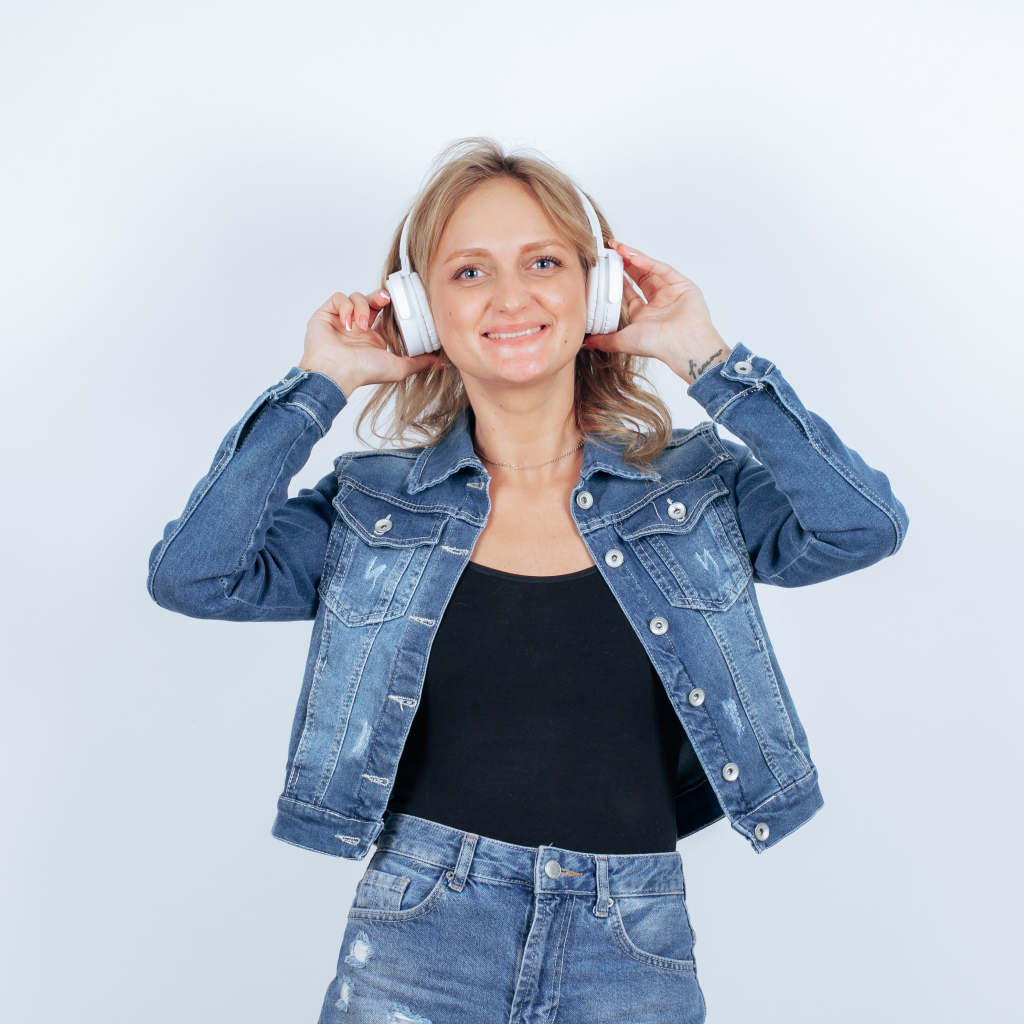 Девушка в джинсовом костюме с наушниками на голове на фоне стены