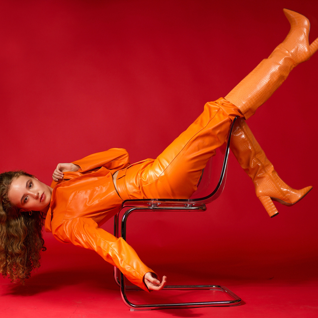 Девушка в кожаном костюме лежит на кресле на красном фоне