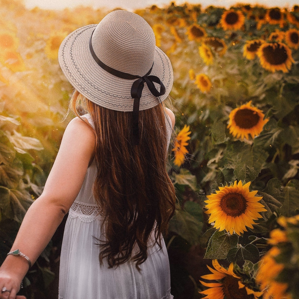 Девушка в белом платье и шляпе идет по полю с подсолнухами