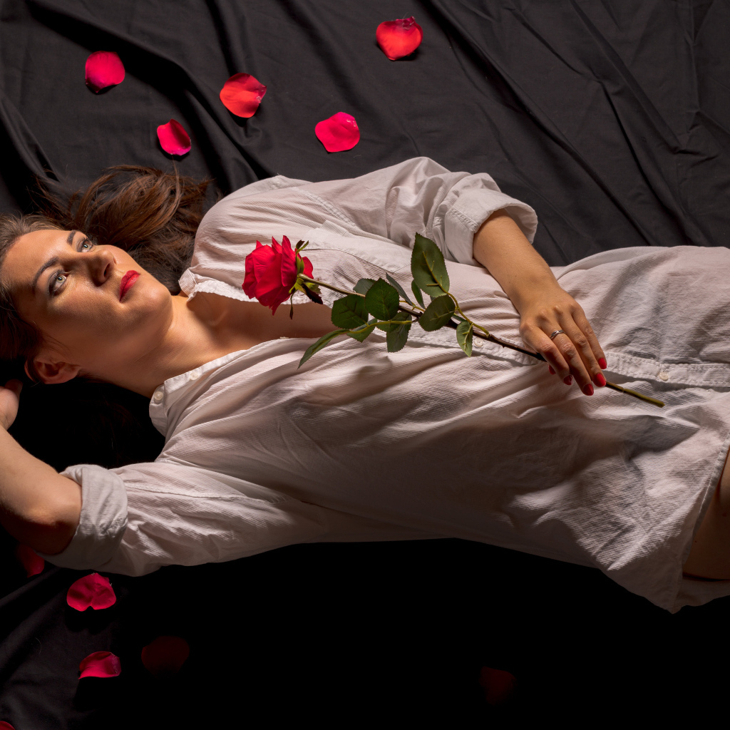 Девушка в белой рубашке с розой в руках лежит на постели
