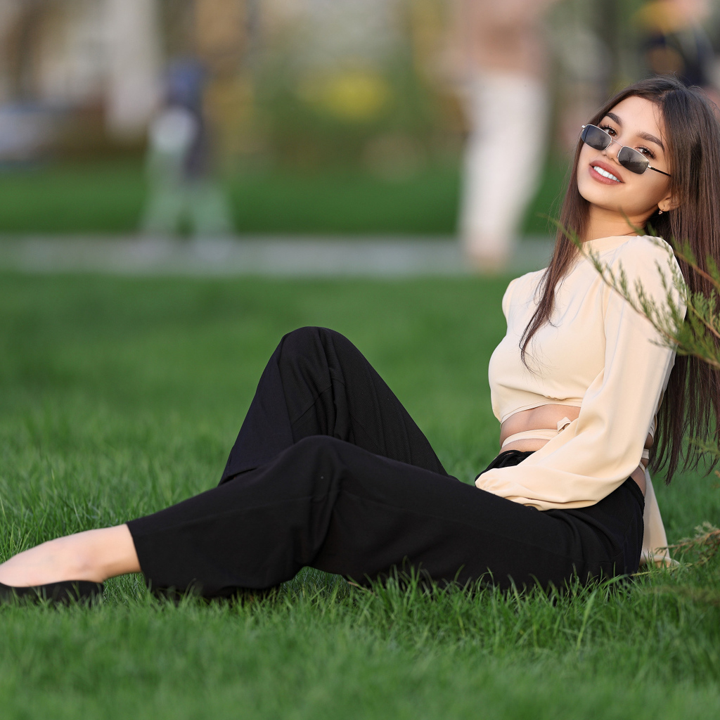 Девушка в черных брюках и блузке сидит на траве