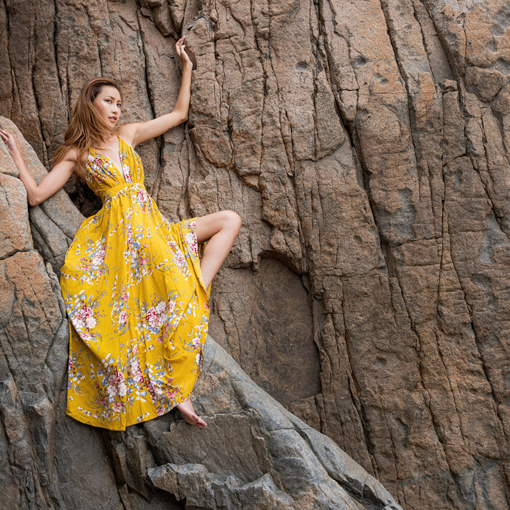 Девушка азиатка в красивом длинном платье позирует на скале