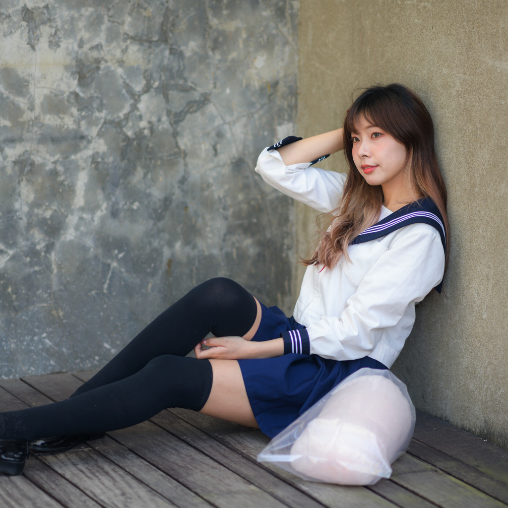 Азиатка в черных чулках сидит у стены