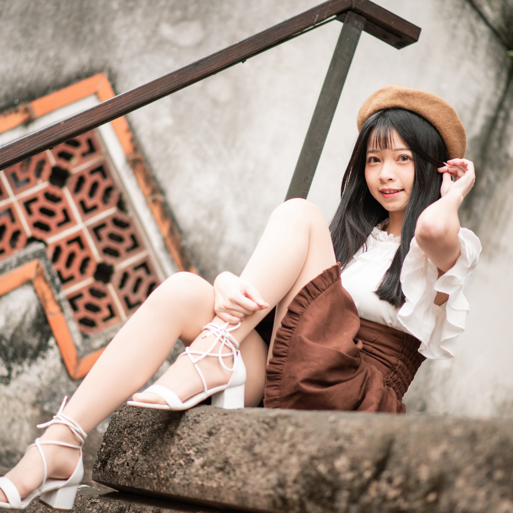 Девушка азиатка в белых туфлях сидит на ступеньках
