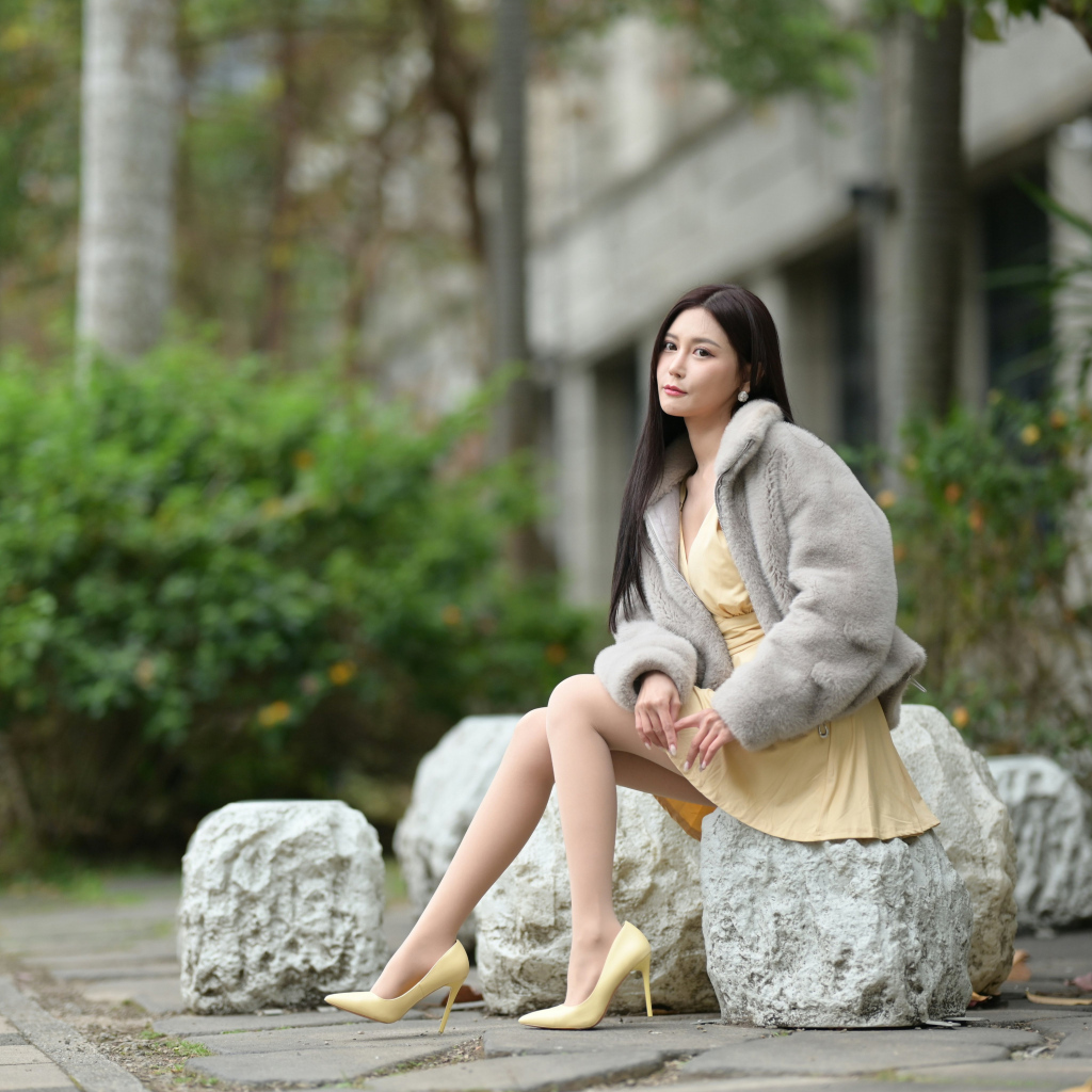 Азиатка в шубе сидит на квадратном камне