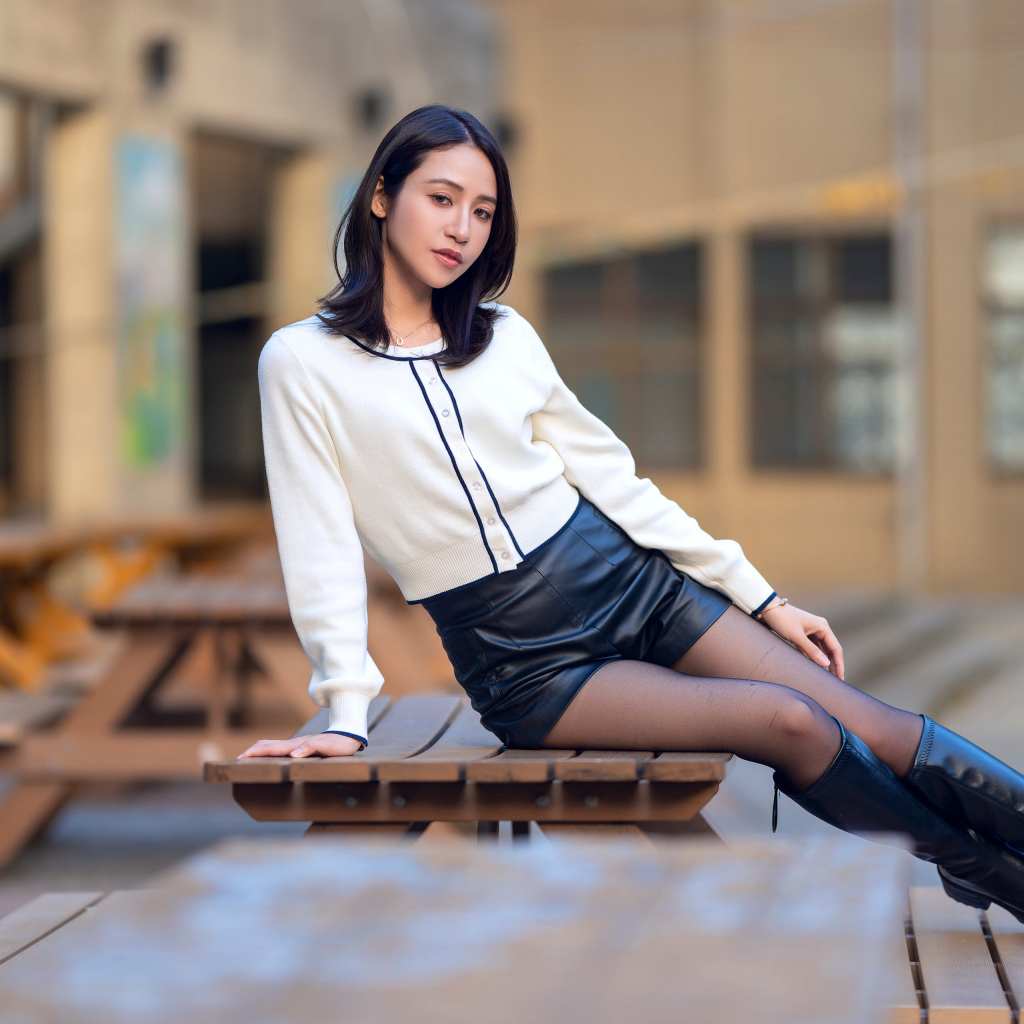 Азиатка в черных кожаных сапогах лежит на деревянном столе