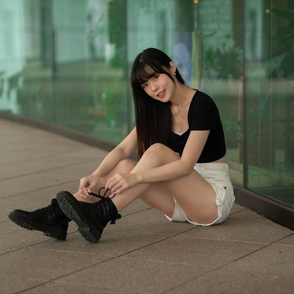 Азиатка в шортах сидит у стеклянной стены