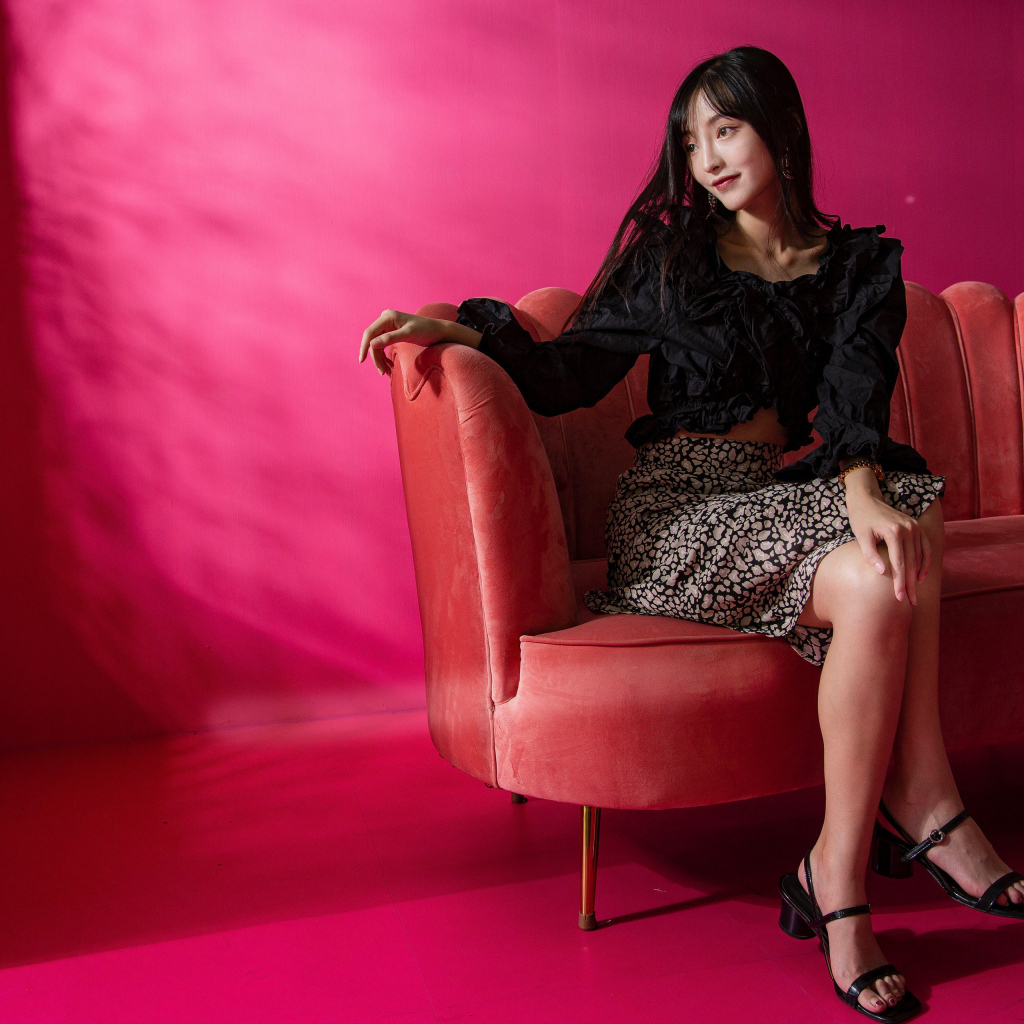 Красивая азиатка сидит на красном диване у окна