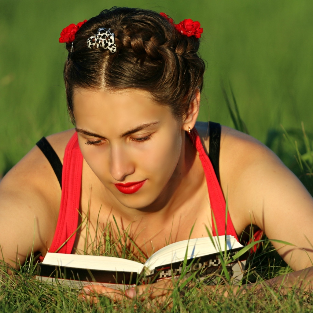 Красивая девушка читает книгу лежа на траве