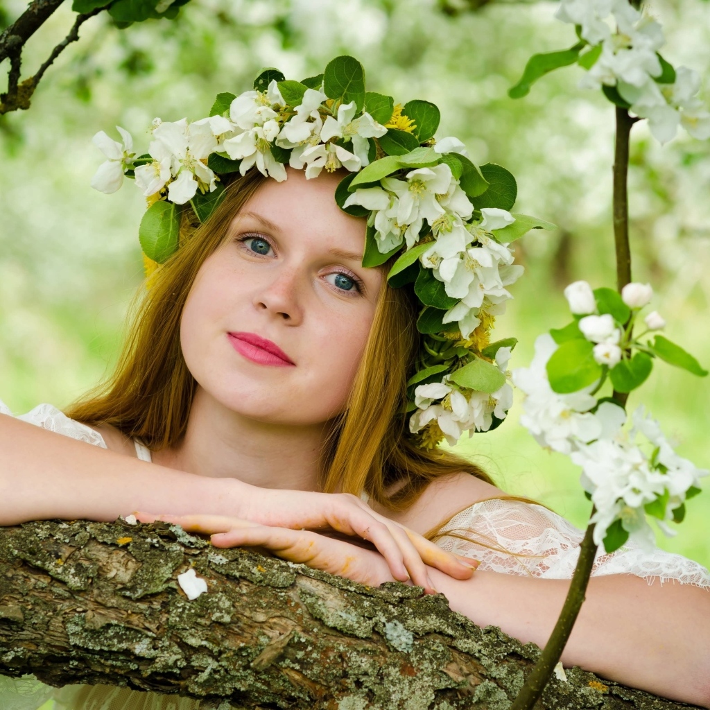 Красивая девушка с венком из цветов на голове у дерева весной