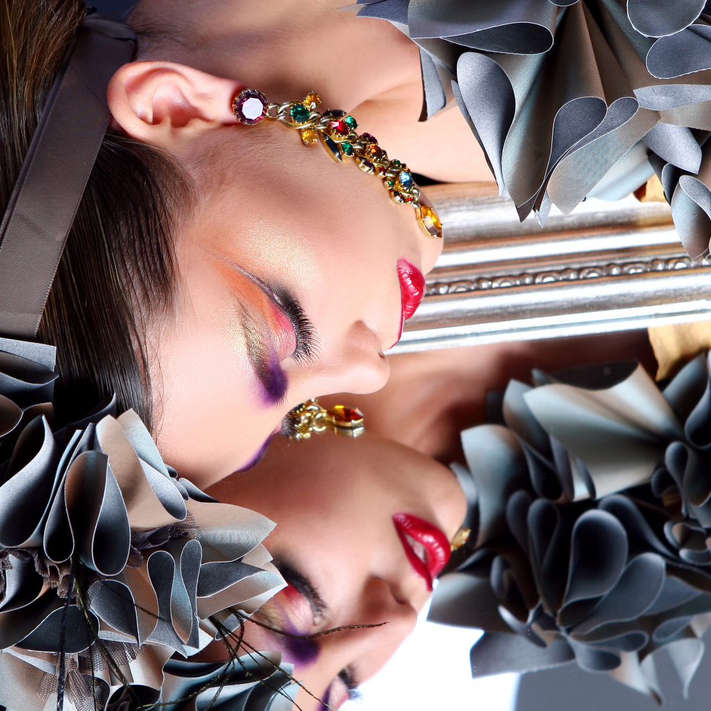 Красивая девушка с ярким макияжем отражается в зеркале