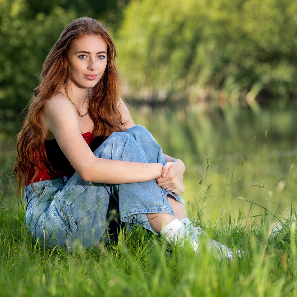 Красивая рыжеволосая девушка сидит в зеленой траве